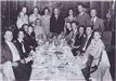 Black and white photo of people gathered around a long dinner table