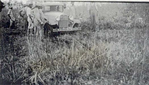 Black and white photo of men and a car parked in a field