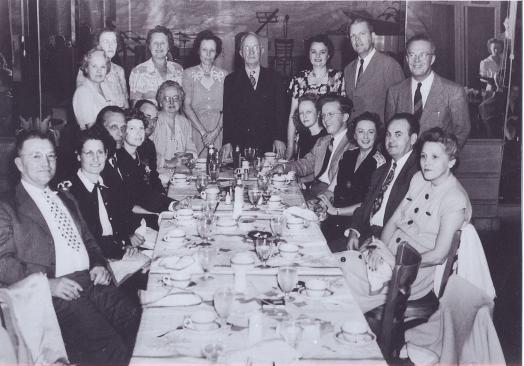 Black and white photo of people gathered around a long dinner table